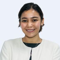 A person wearing a white blazer and a black top, smiling in front of a plain background.
