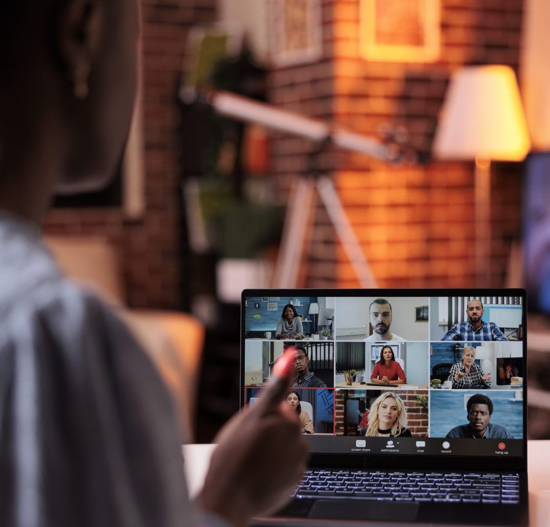 Person participating in a video conference on a laptop, with eight people visible on the screen in a home office setting.