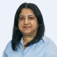 A person with shoulder-length black hair is wearing a light blue shirt against a plain background.