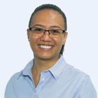 Person smiling, wearing glasses and a light blue collared shirt with a white background.