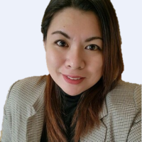 A woman with long hair and a checkered blazer smiles at the camera against a light background.