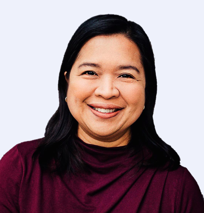 A person with long dark hair, wearing a maroon top, smiles at the camera against a plain background.
