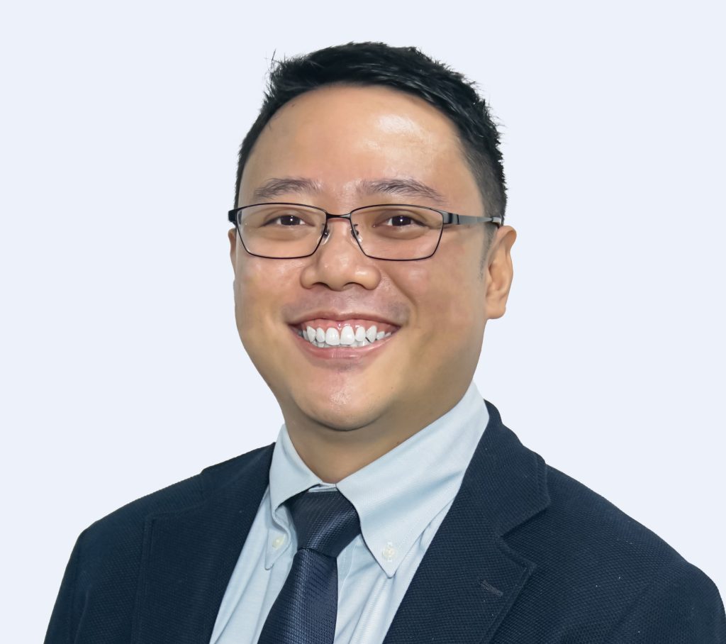 Smiling man in glasses wearing a suit and blue tie against a light background.