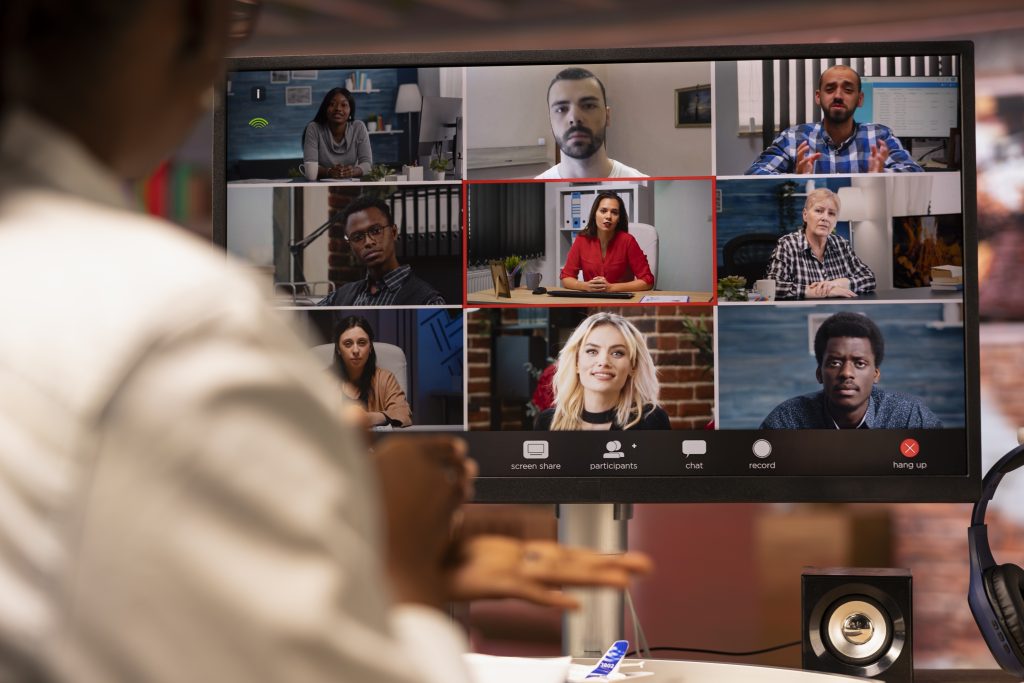 Person participating in a video conference call, with nine diverse people displayed on a computer screen in a virtual meeting.
